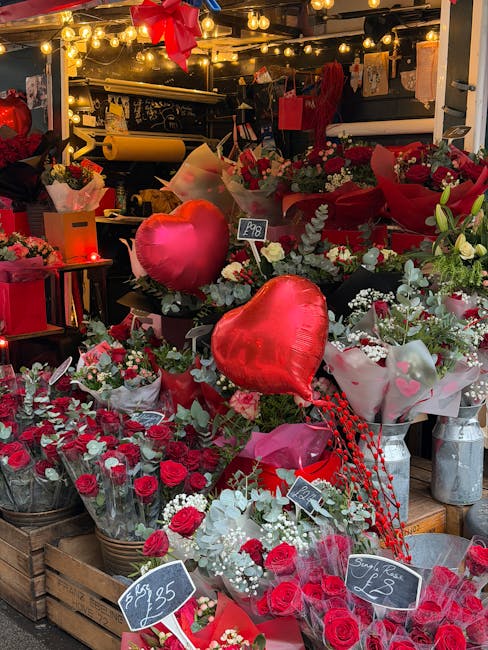 A festive flower display at a flower shop in Crofton Park, featuring an array of fresh red roses, white flowers, and greenery arranged in baskets and bouquets. Prominently, several shiny red heart-sha