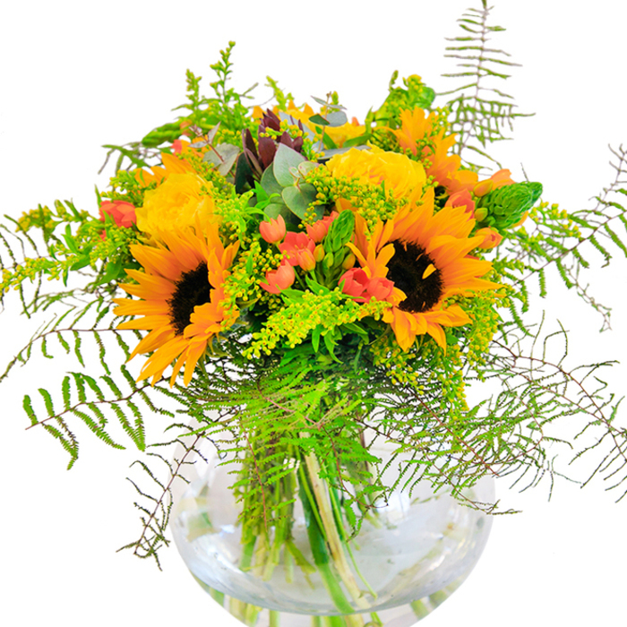 Bringing a touch of Crofton Park's local colour and vibrancy into any home, this striking bouquet is an artistic arrangement that beautifully blends dynamic summer hues with carefully chosen textures. Towering sunflowers, their golden petals radiating around deep, textured centers, evoke a sense of boundless sunshine and optimism, brightening rooms just as the morning light fills Stondon Park. Embracing these are lush, spiralled yellow garden roses, their soft layers and sophisticated form capturing the elegance of a garden in full bloom. Pops of lively red Hypericum berries are interspersed throughout, their glossy finish and cheerful tones echoing the vivid flowers spilling over fences along Brockley Grove. Fern fronds tumble gracefully downward, while fine, airy green filler and subtle stems of eucalyptus add depth, movement, and a rustic, fresh-cut feeling. All elements nestle together in a round, transparent glass vase, where each submerged stem forms a tapestry of lively greens and shimmering water. The texture contrasts abound-from the satiny petals and plush sunflowers to the crisp greens and pillowy fillers. A subtle scent floats upward: a delicate blend of earthy greenery and soft rose, reminiscent of a Crofton Park stroll in high summer. Crafted for milestone celebrations or to surprise a loved one with a rush of happiness, this bouquet is a visual and sensory joy, testament to the creativity and personal touch at the heart of Flowers Crofton Park's floristry.